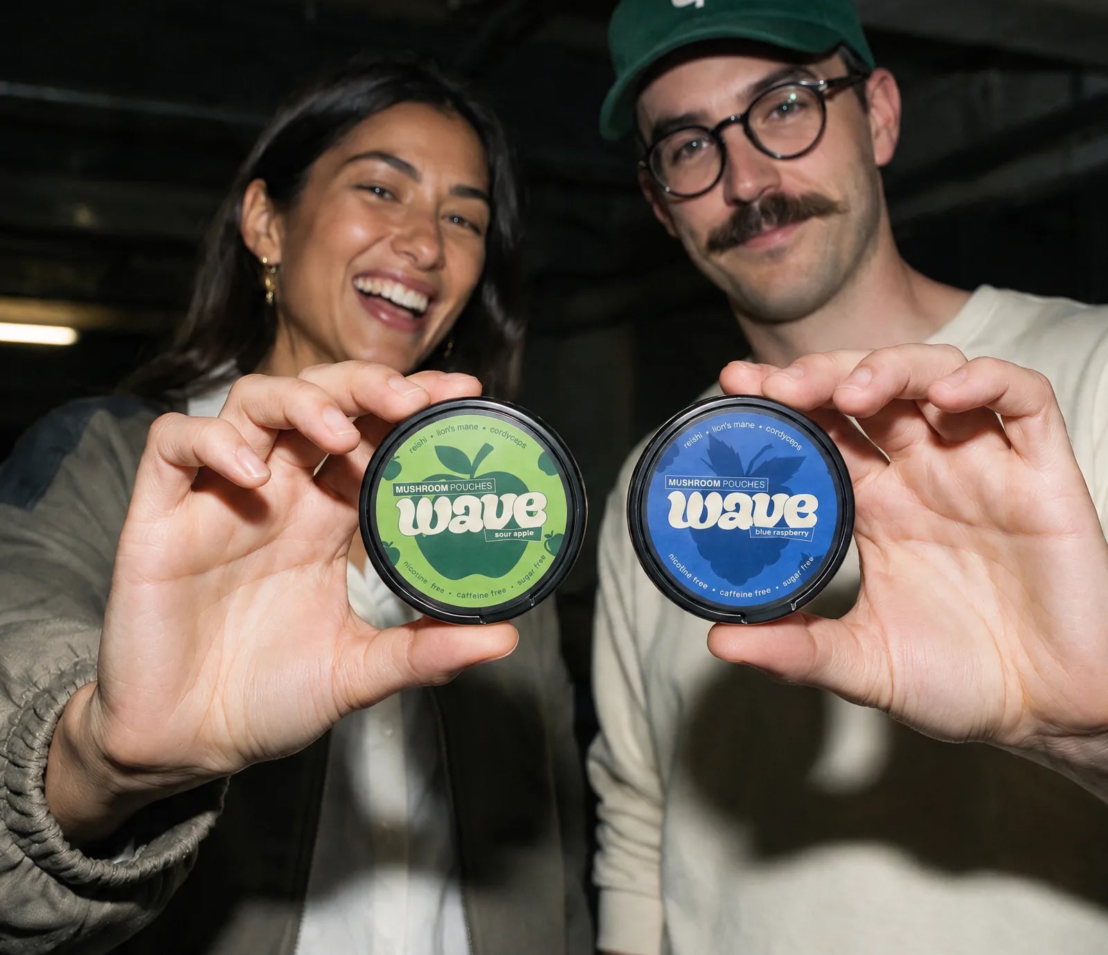 Two friends in a garage holding a Sour Apple and a Blue Raspberry WAVE can up to the camera