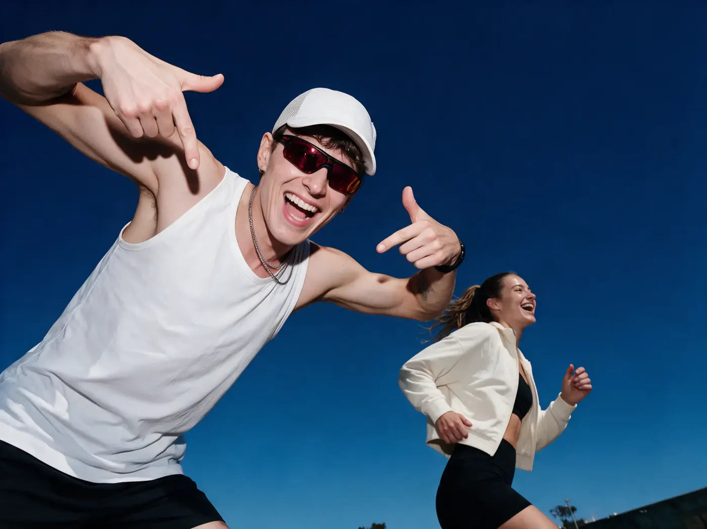 A man in a white cap laughing while a woman runs behind him under a blue sky