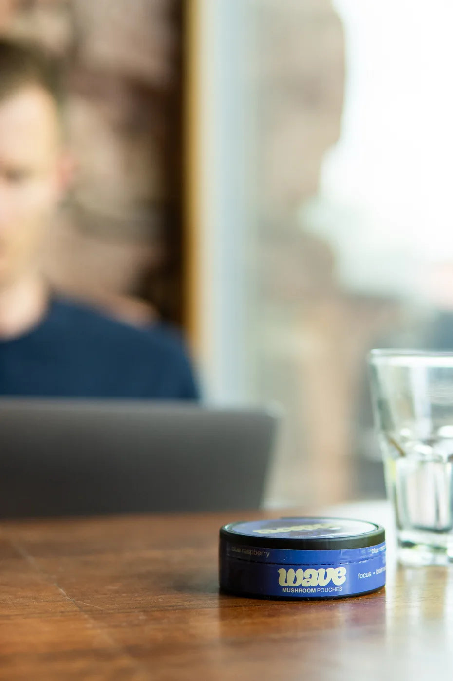 WAVE can on a wooden café table, a man with a laptop in the background