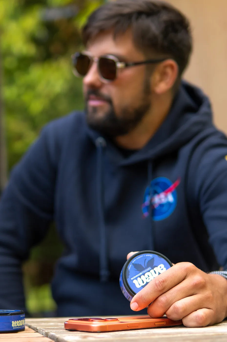 Man in sunglasses and a navy hoodie at an outdoor table, a WAVE can in his hand